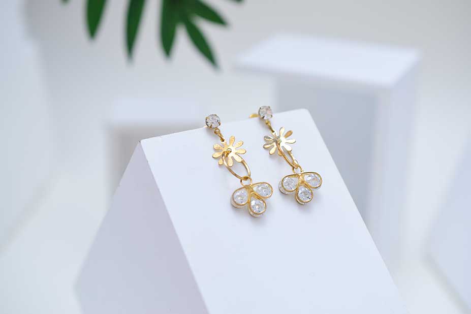 Gold flower drop earrings on a white display block