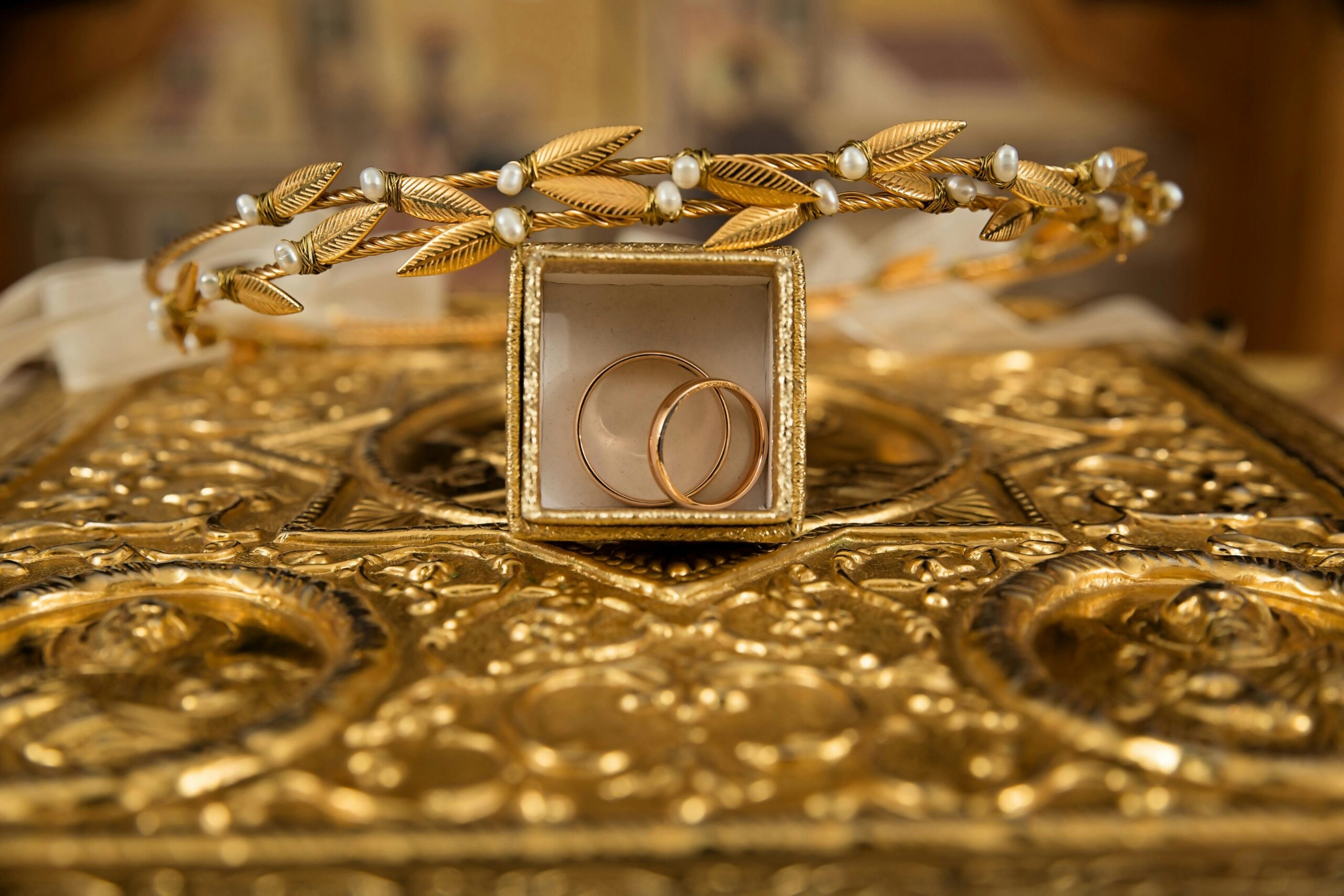 Gold wedding rings in a jewelry box surrounded by ornate gold jewelry